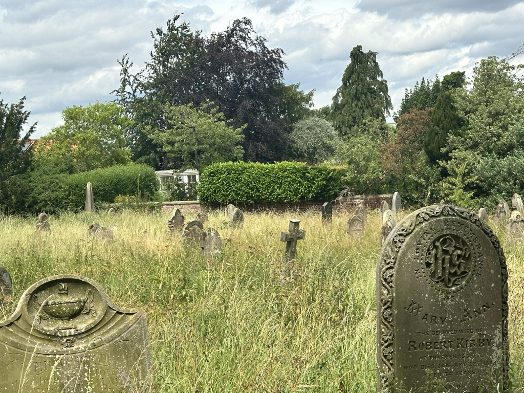 St Andrew’s churchyard, Rillington, with historic gravestones among long summer grass.